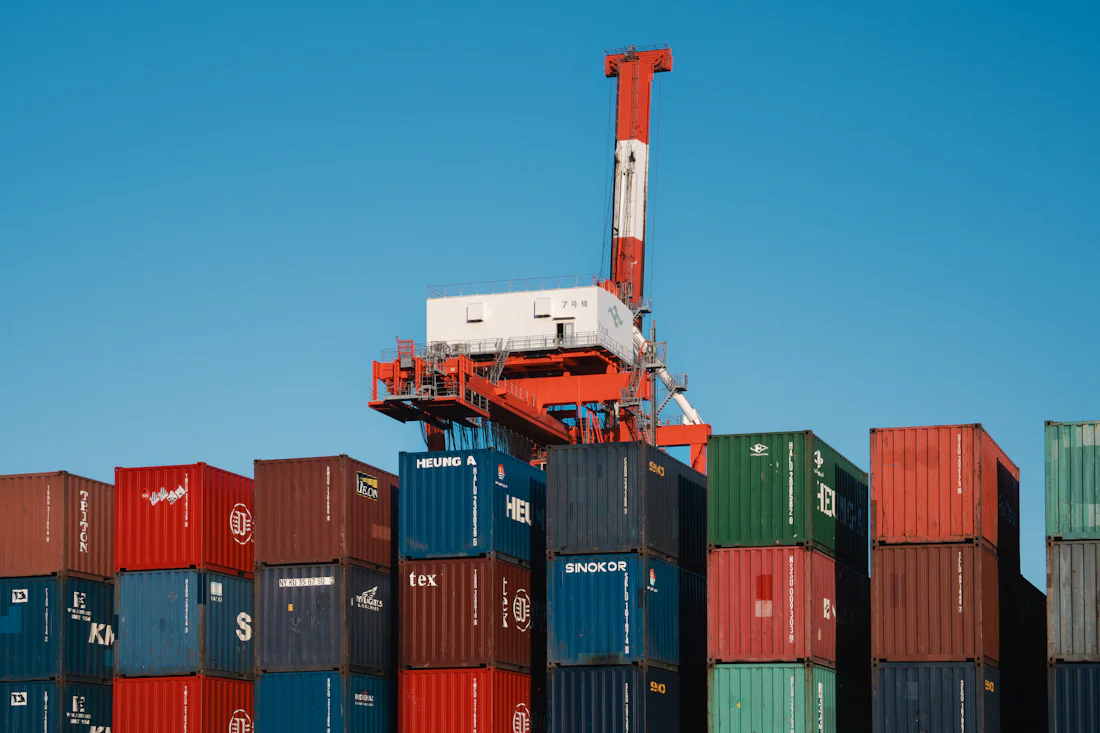 A gantry crane standing over a stack of shipping containers against a clear sky